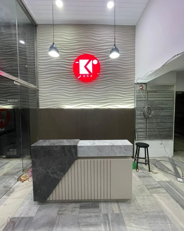 Two-tone marble reception desk beneath an illuminated wave-panel wall and building directory